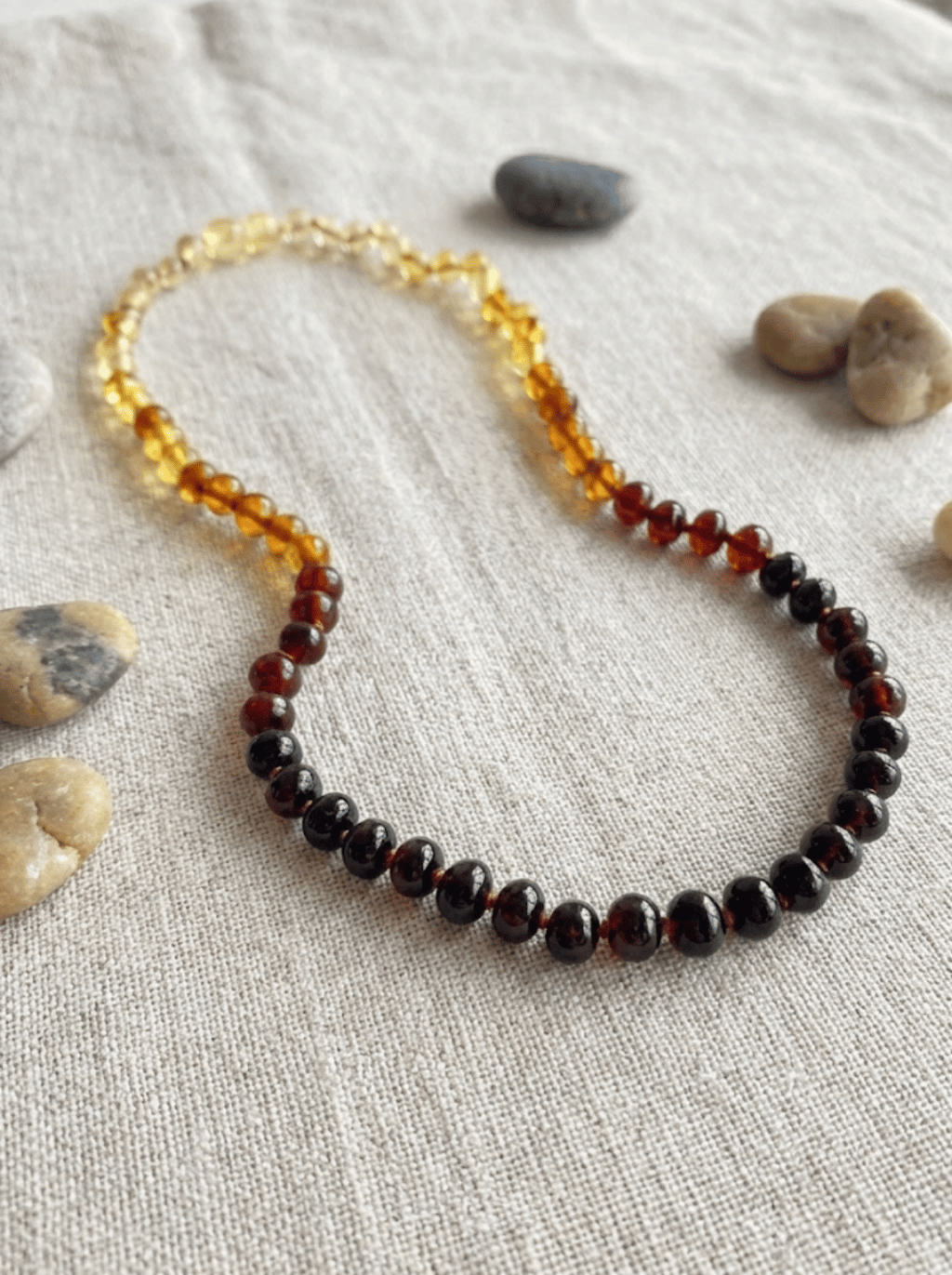 Necklace with amber and red beads on a textured surface with stones.