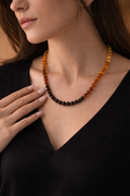 Close-up of a person wearing a beaded necklace with amber and black beads.