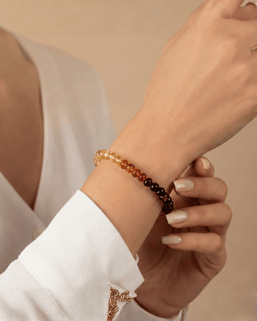 Hand wearing a beaded bracelet on a beige background